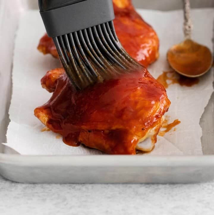 A close-up of chicken being basted with BBQ sauce