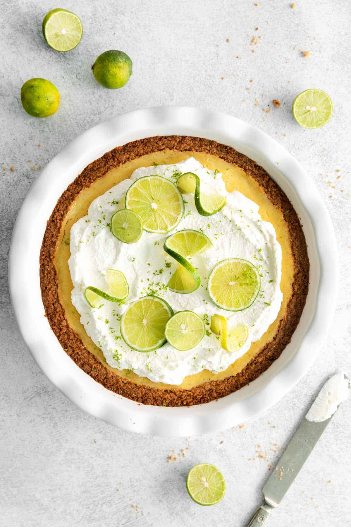 Key lime pie on a countertop, surrounded by fresh limes and a knife