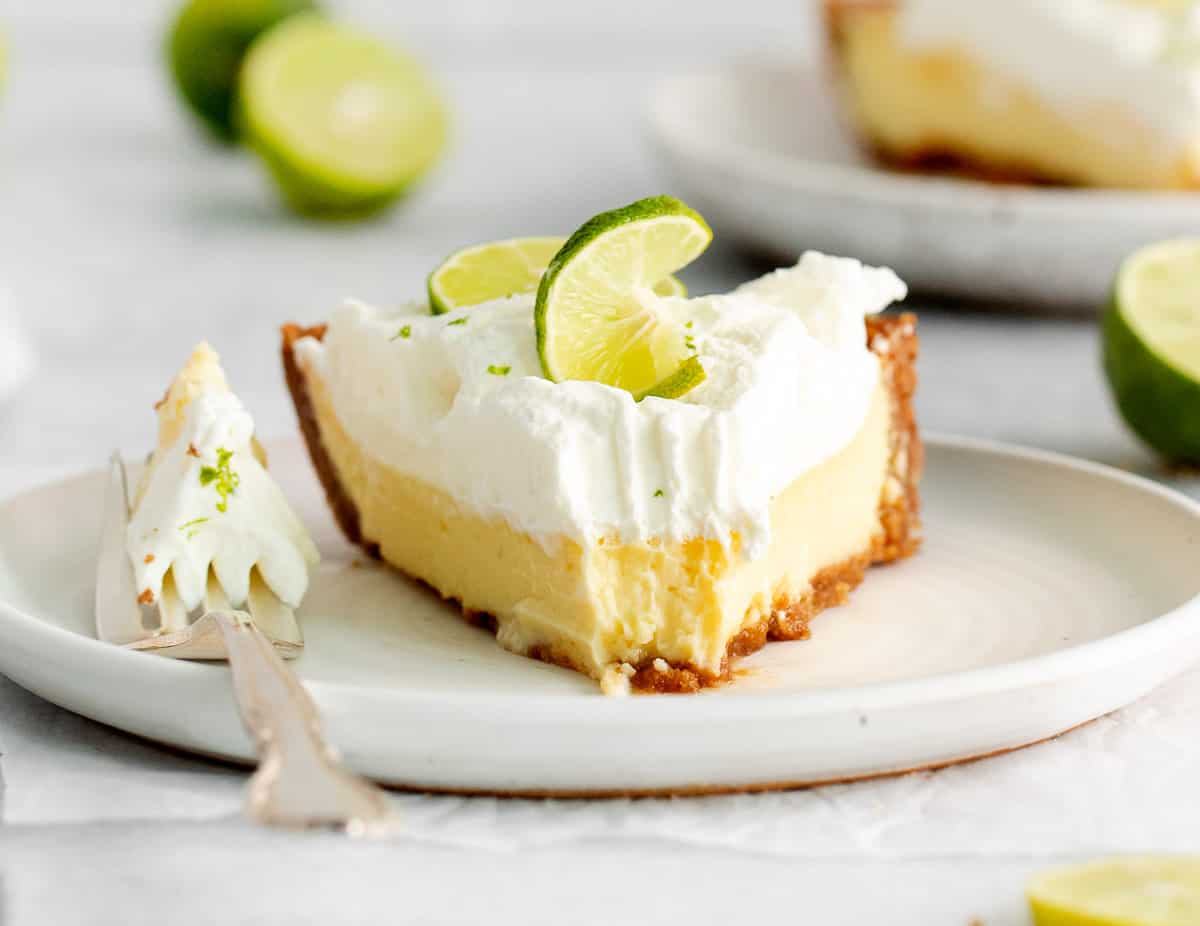 A slice of key lime pie on a plate with a bite taken out of it