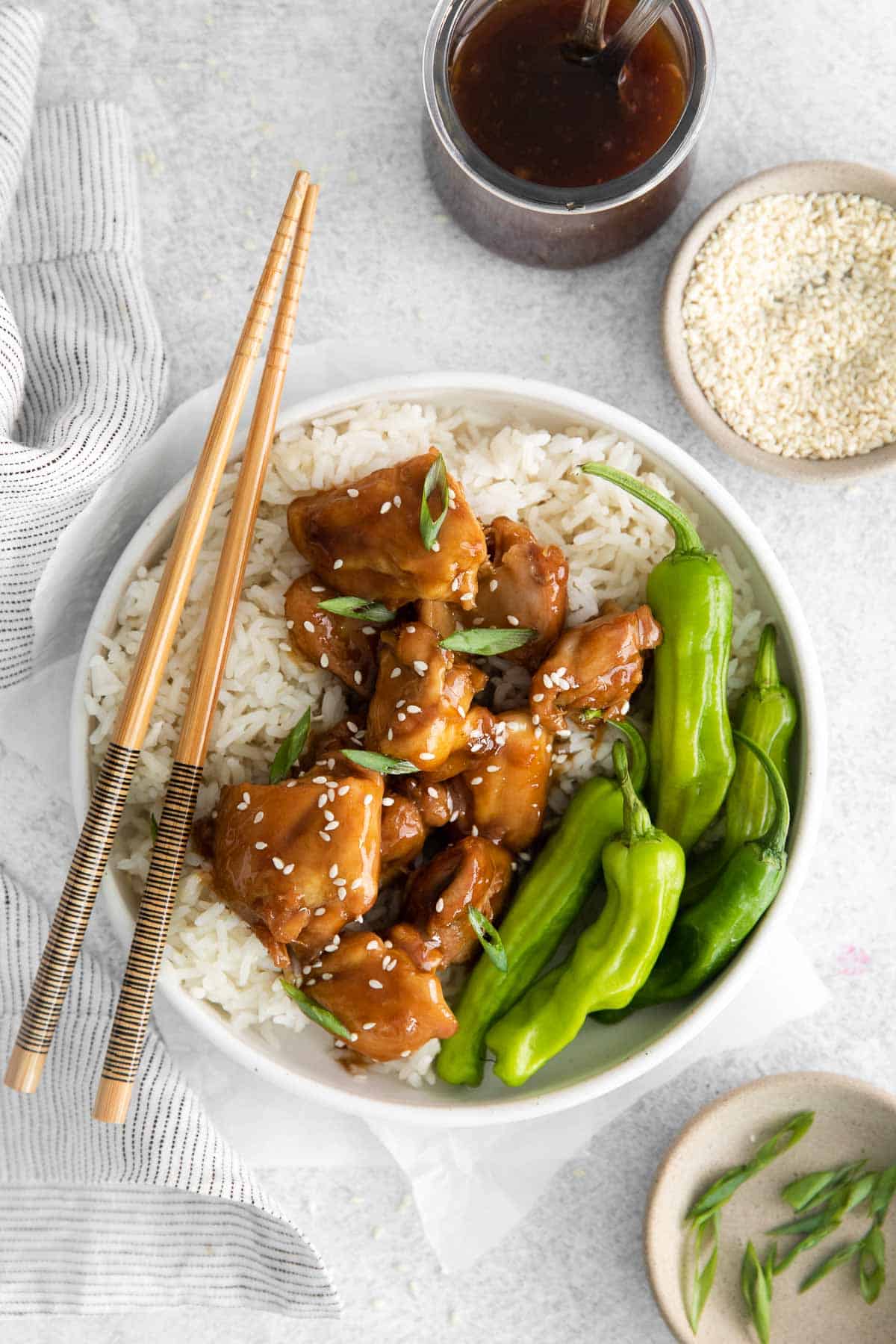 A bowl of chicken, rice, snap peas, and teriyaki sauce with chopsticks on the side