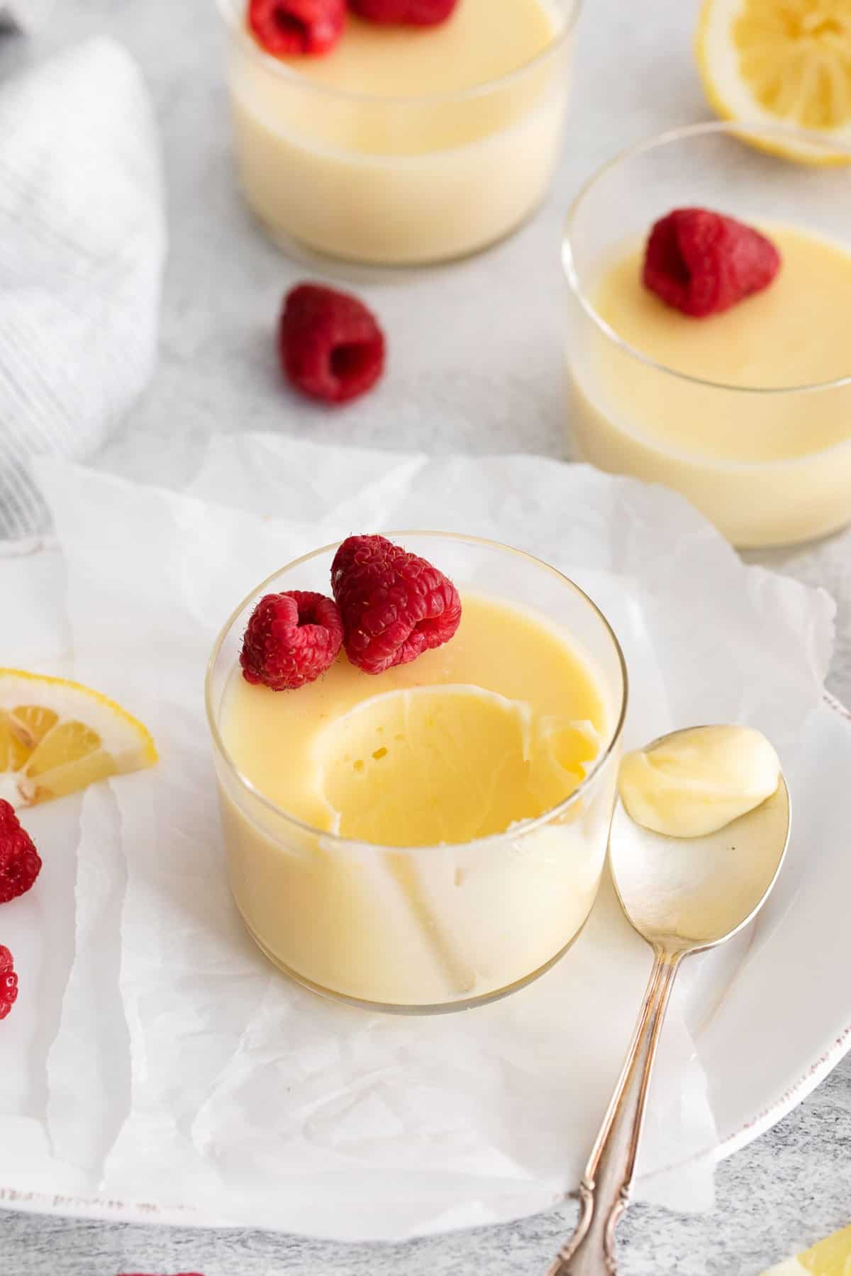 Lemon posset in a small dish with a bite taken out of it, with raspberries on top and a spoon next to it