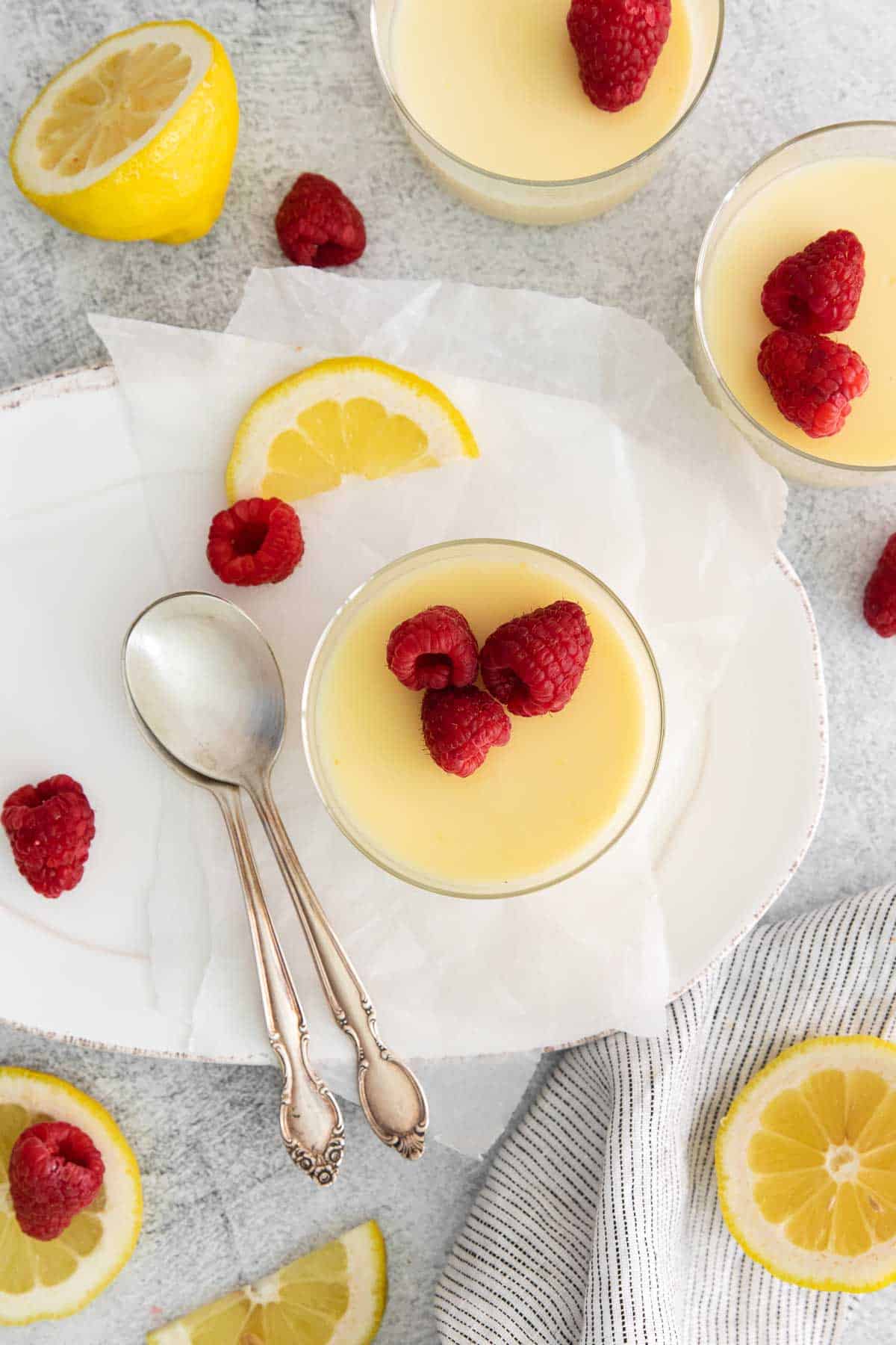 An overhead shot of lemon posset in a small dish, with raspberries on top and a spoon next to it