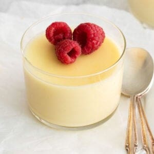 Lemon posset in a small dish, with raspberries on top and a spoon next to it