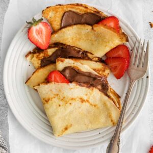 Crepes on a plate, filled with Nutella and strawberries