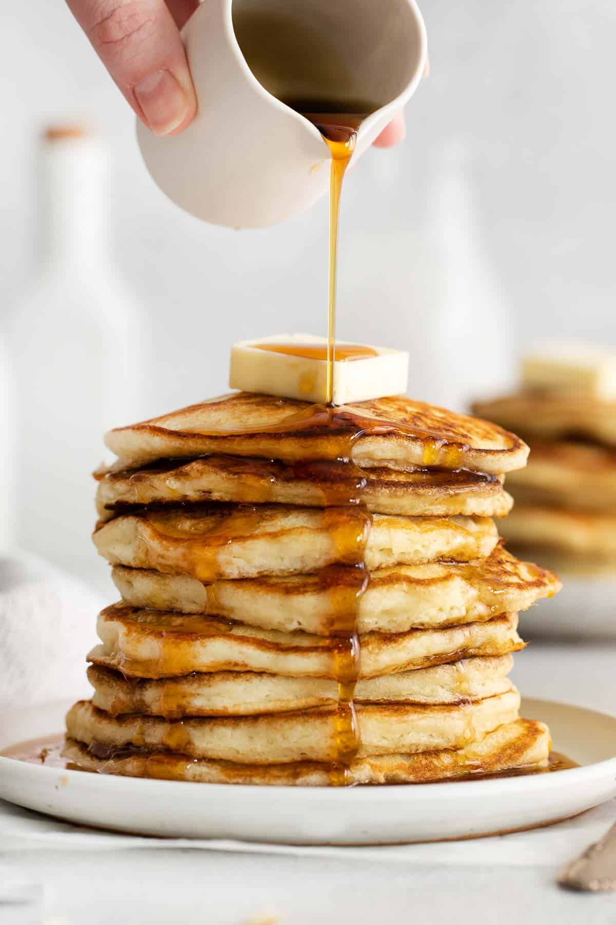 Stack of gluten-free pancakes on a plate with a pat of butter on top and syrup being poured over it
