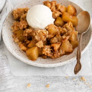 Gluten-free apple crumble on a plate with a spoon next to it and a scoop of ice cream on top