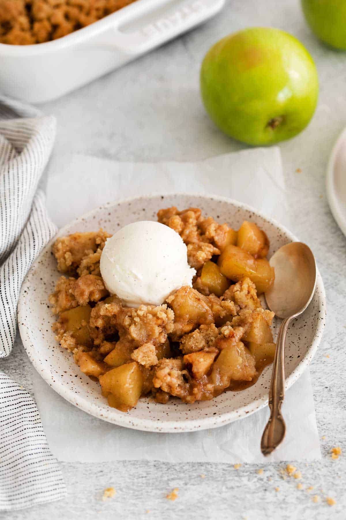 A serving of gluten-free apple crumble on a plate, with a scoop of vanilla ice cream on top and a spoon next to it