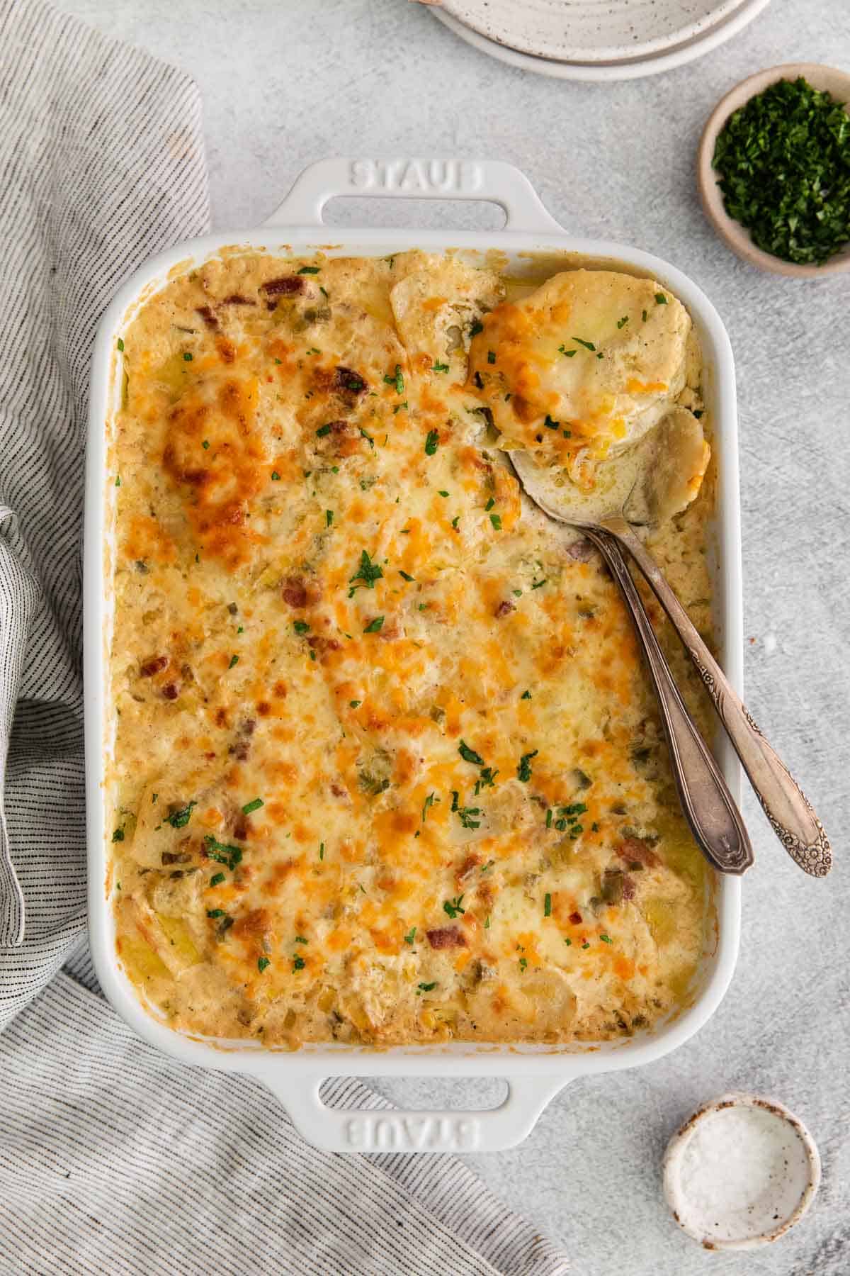 Scalloped potatoes in a baking dish, with a serving spoon scooping a portion from the corner of the dish
