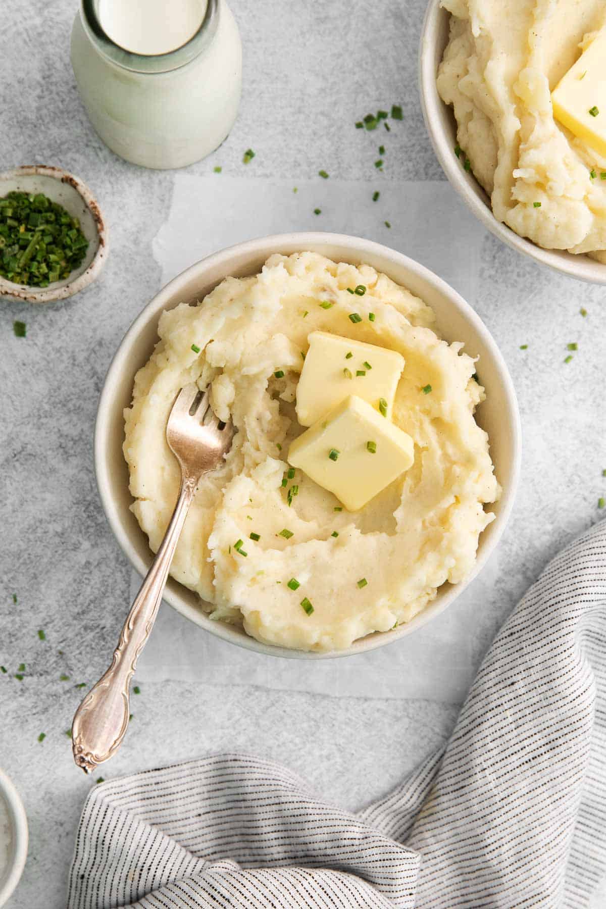 Gluten-free mashed potatoes in a bowl, with a pat of butter, parlsey, and a serving spoon