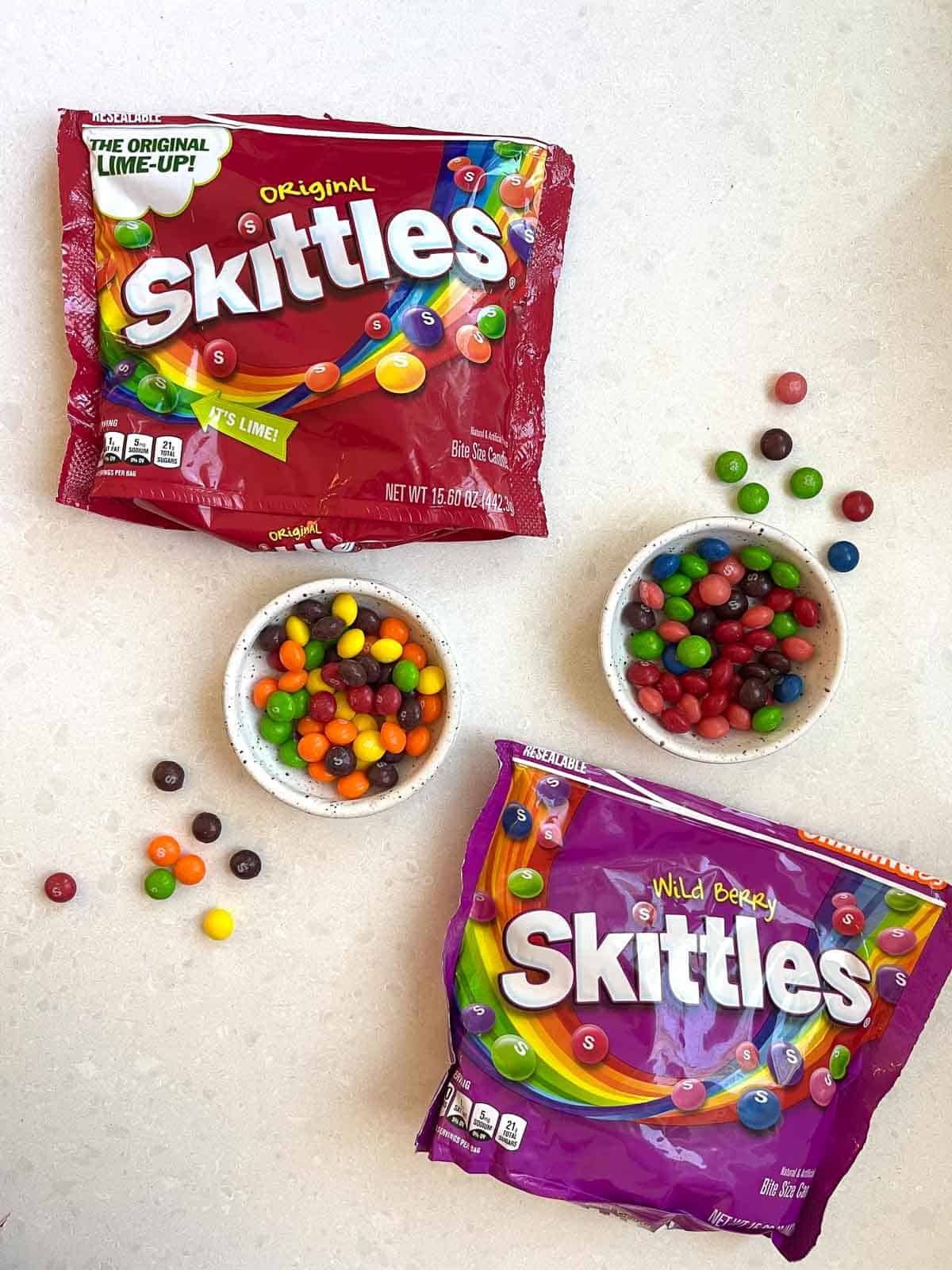 2 bags of skittles on white counter with 2 bowls of skittles