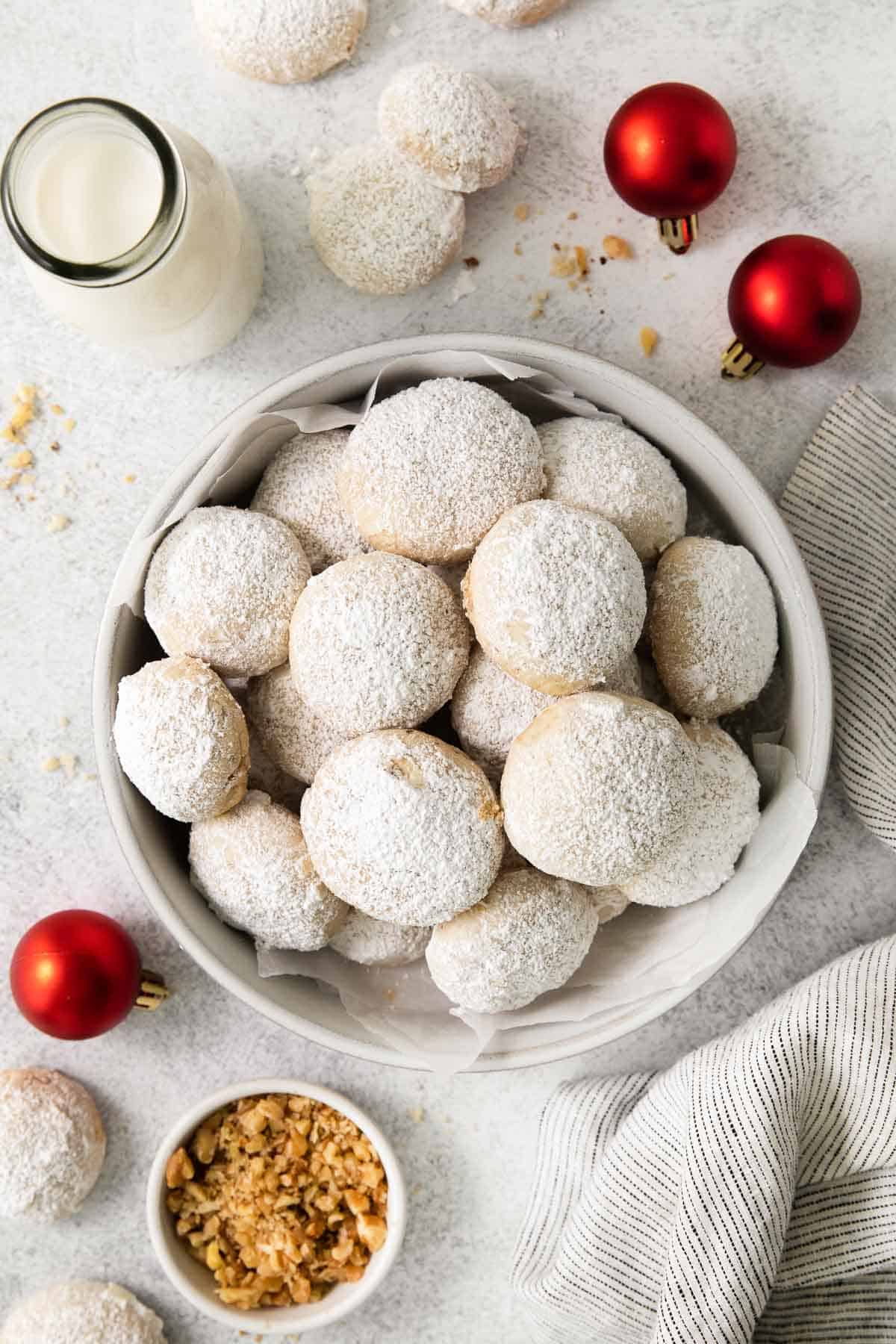gluten-free snowball cookies in a bowl with ornaments surrounding the bowl