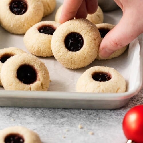 Gluten-free thumbprint cookies on a tray with a hand picking up one cookie