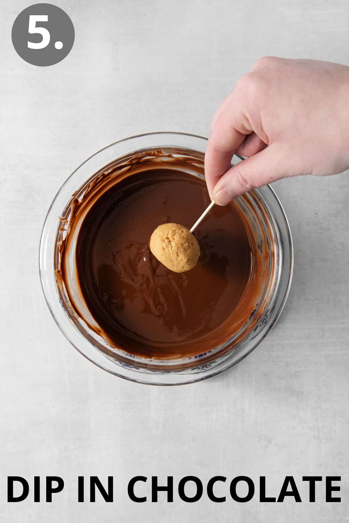 One peanut butter ball on a toothpick being dipped in melted chocolate