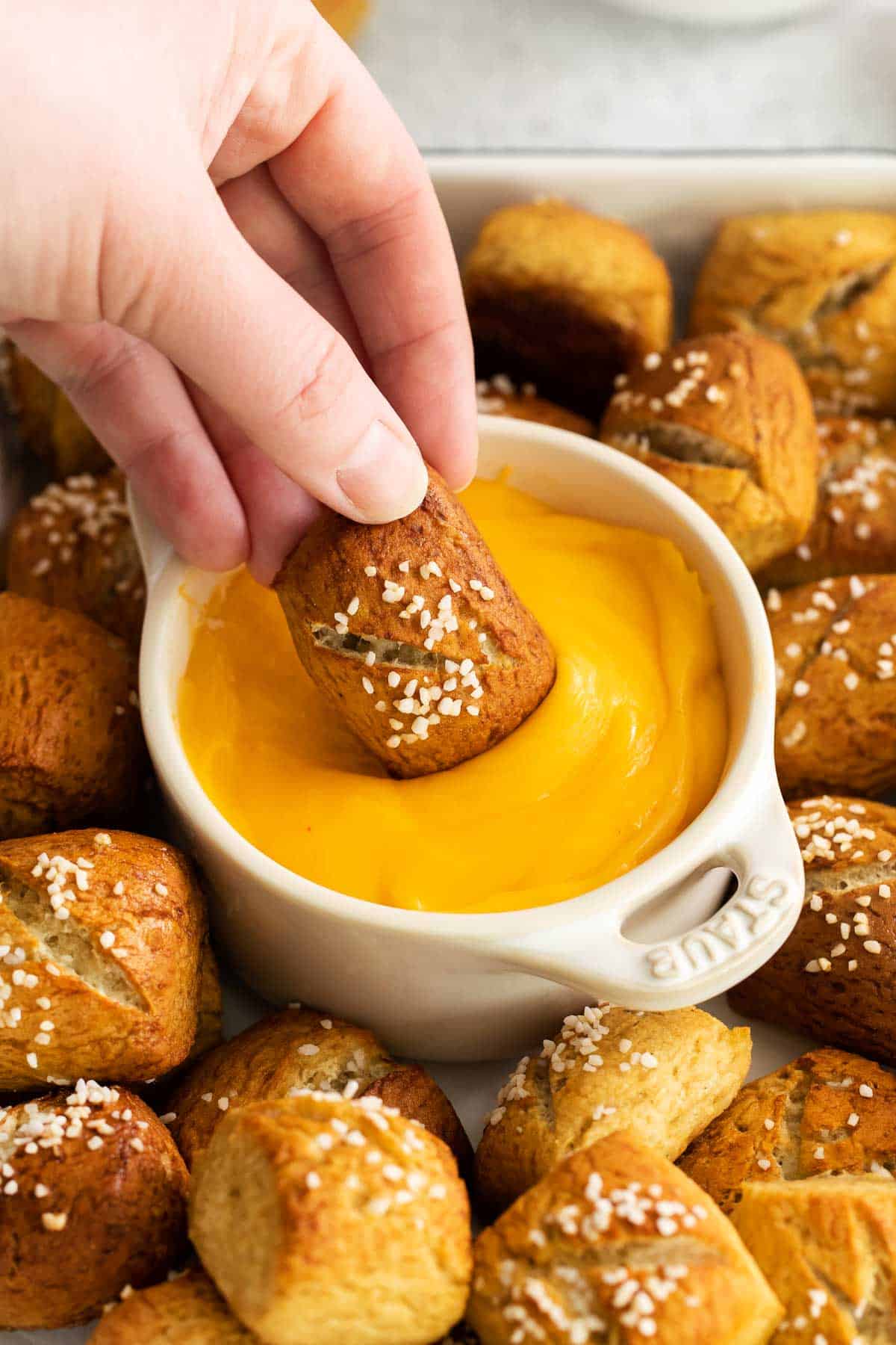 a hand dipping a pretzel in cheese sauce