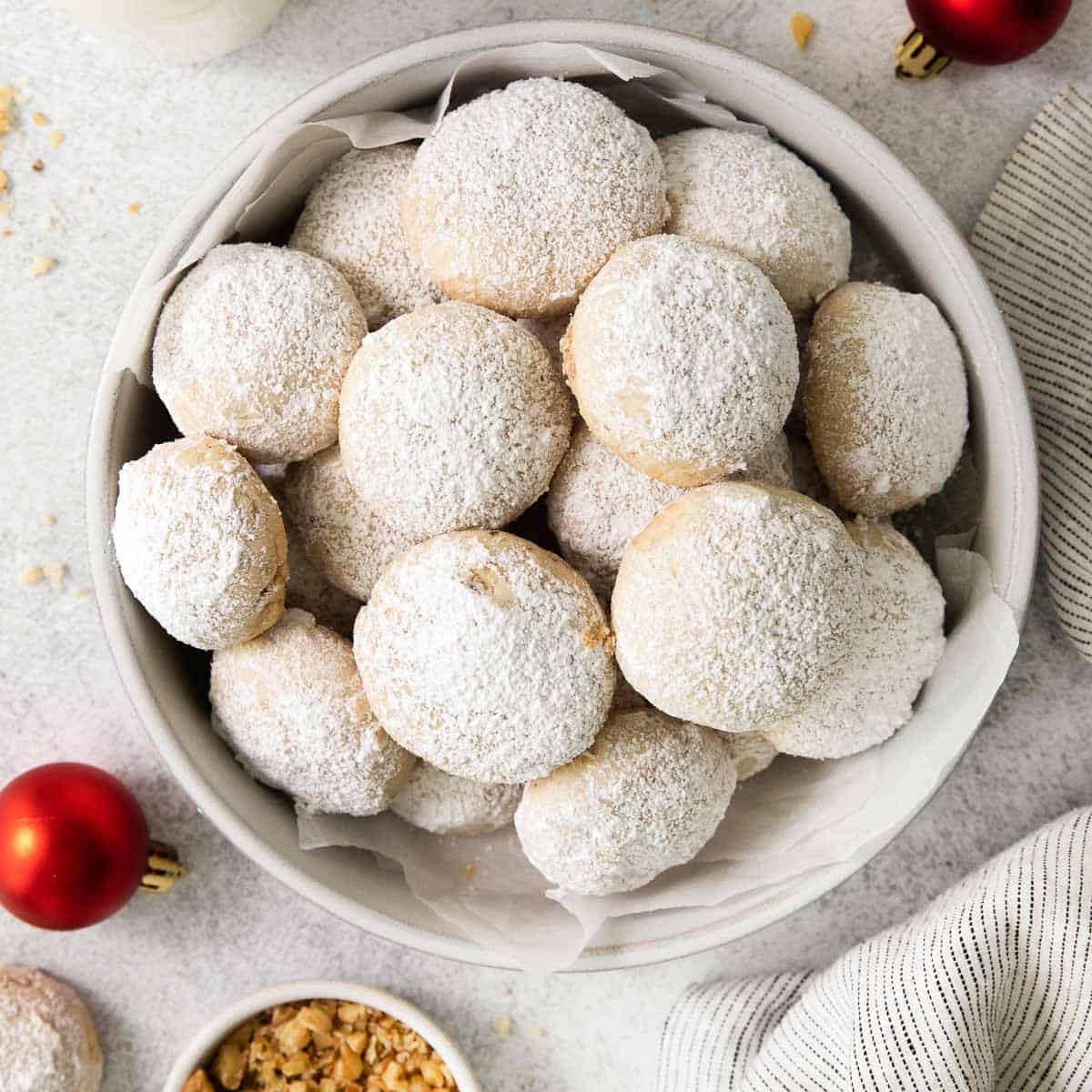 gluten-free snowball cookies in a bowl with ornaments surrounding the bowl