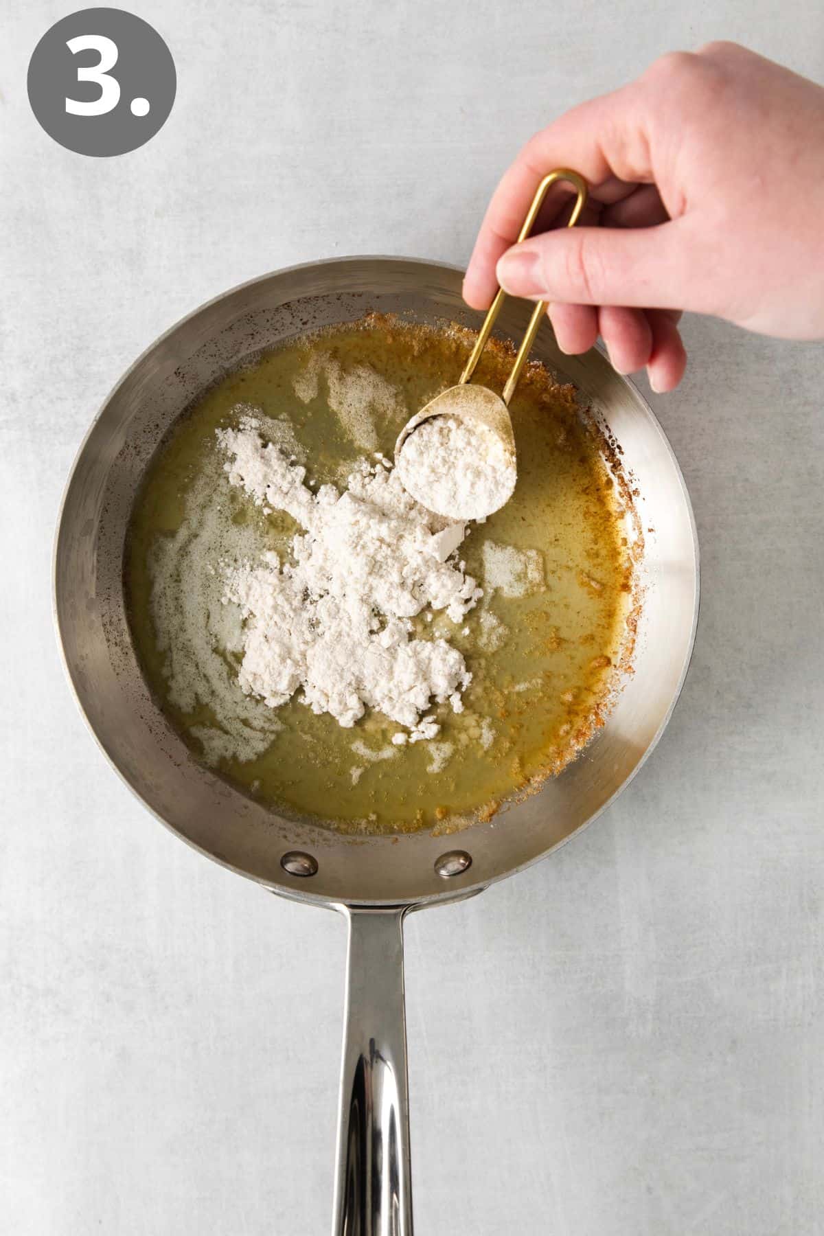 Flour being poured into a skillet with melted butter