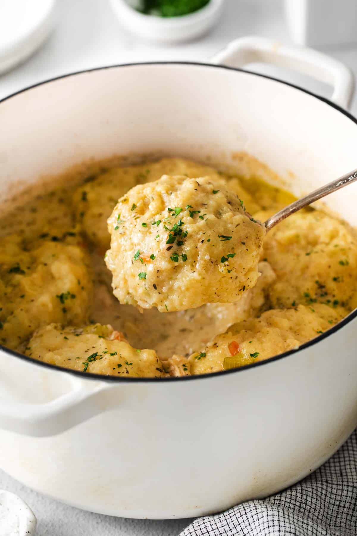 A close-up photo of chicken and dumplings in a baking dish with a spoon scooping out a serving