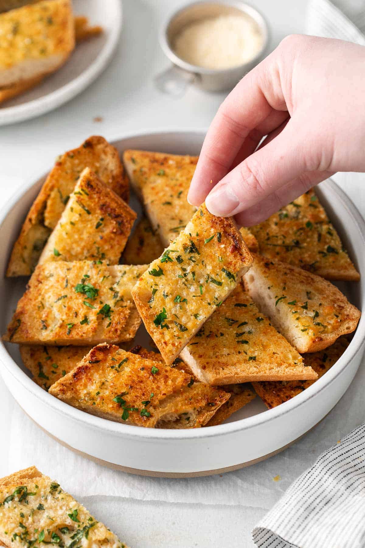 Gluten-free garlic bread sliced in a bowl with a hand picking up a piece