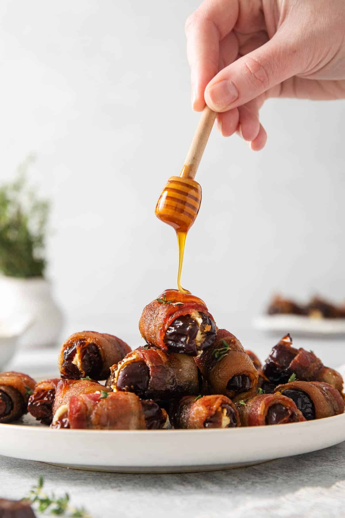 Bacon-wrapped dates on a plate, and a hand drizzling honey over them