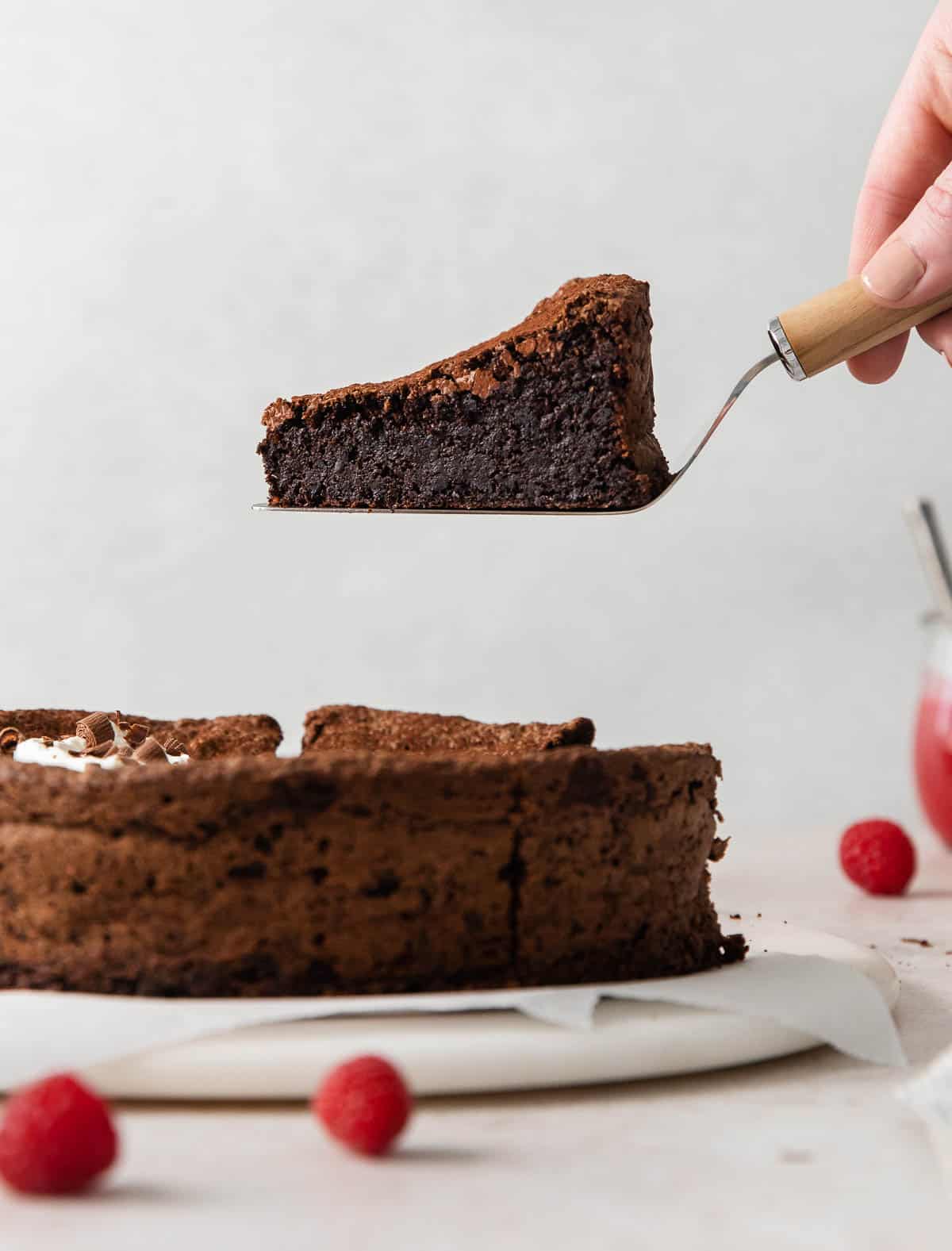 A side view of flourless chocolate torte, and a hand serving up a slice from the platter