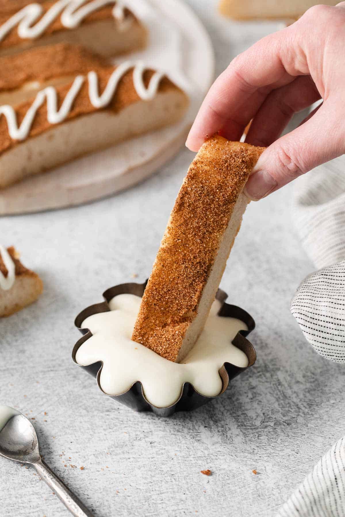 A hand dipping a cinnamon breadstick in glaze
