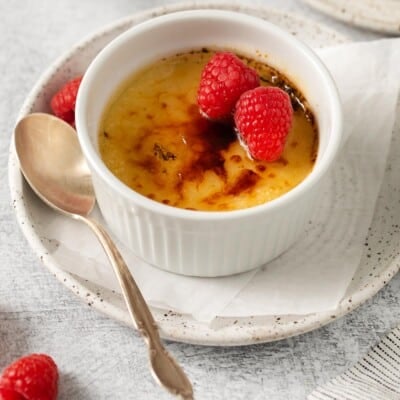 Dairy-free creme brulee in a ramekin, with raspberries on top and a spoon on the side