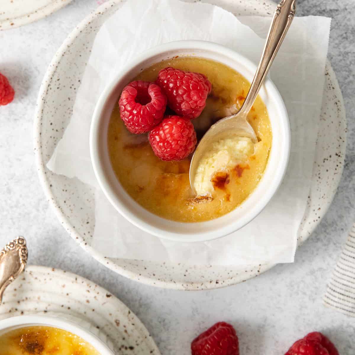 Dairy-free creme brulee in a ramekin, with raspberries on top and a spoon dipping into the ramekin