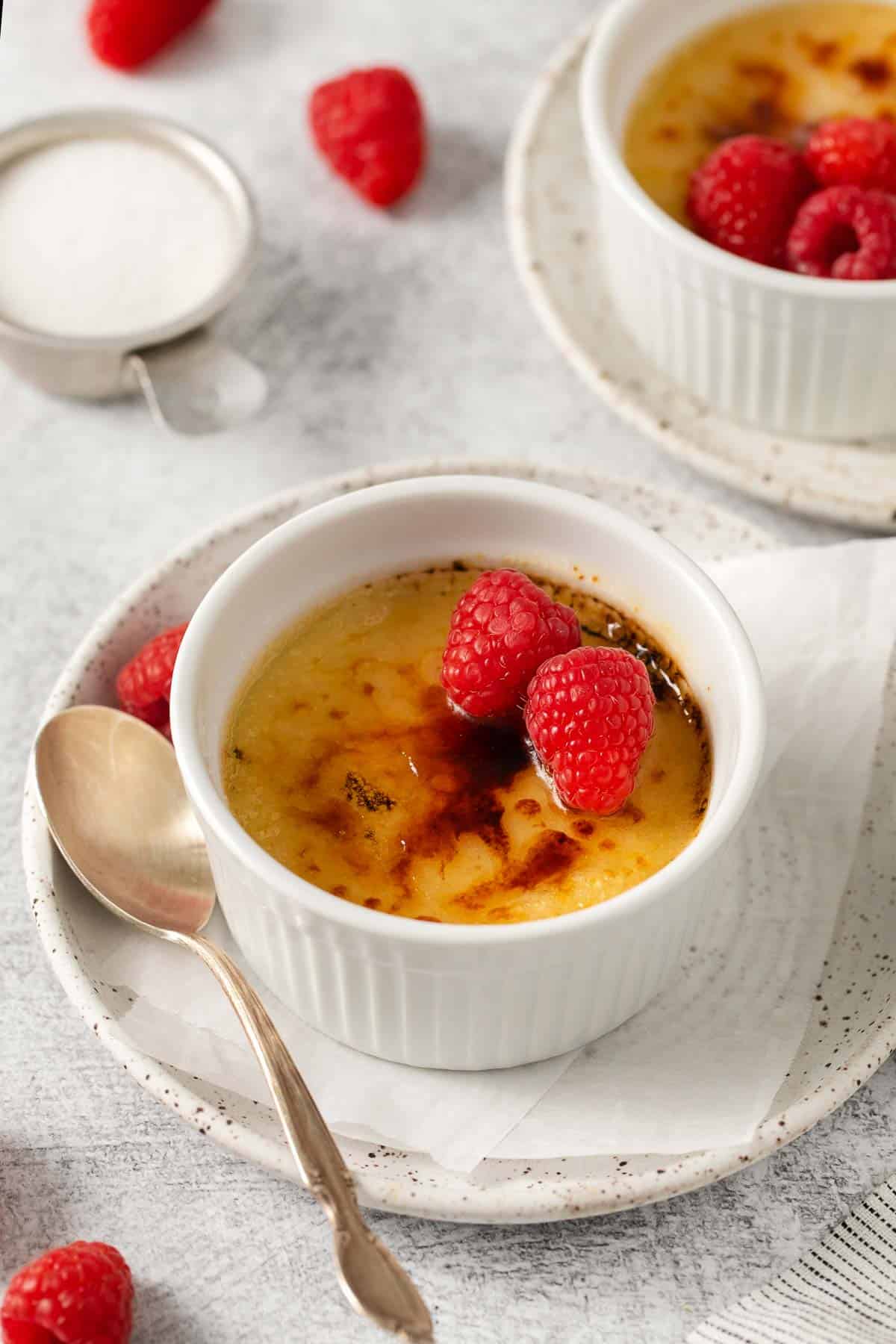 Dairy-free creme brulee in a ramekin, with raspberries on top and a spoon on the side