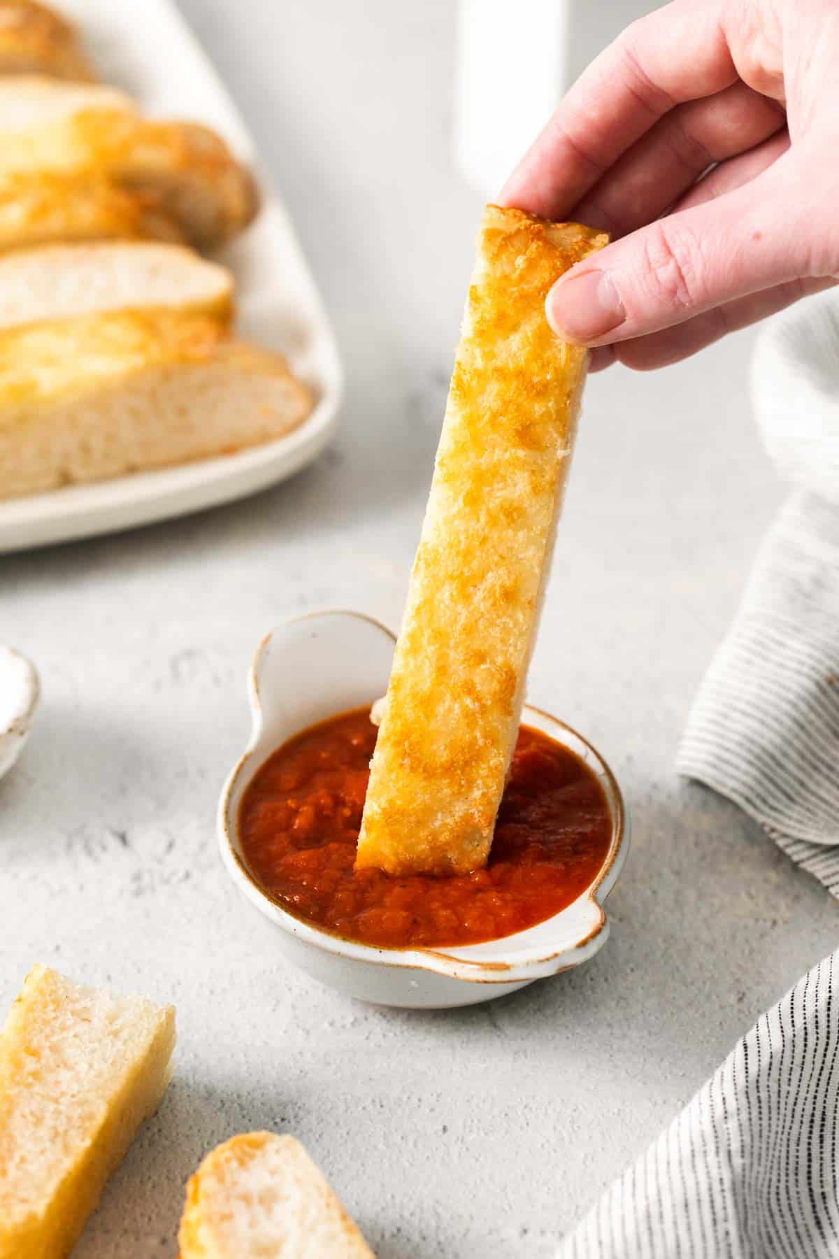 A hand dipping a breadstick in sauce