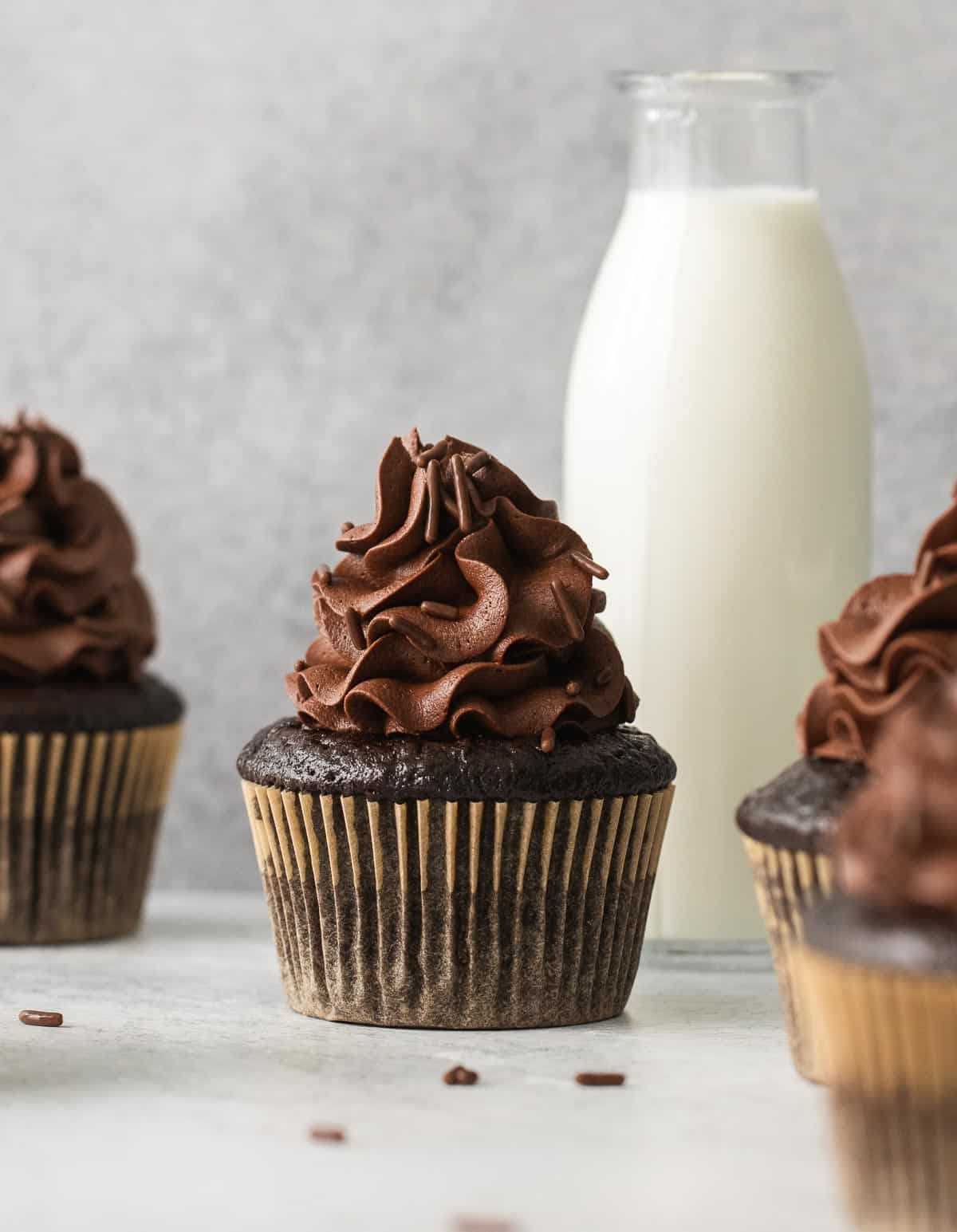 A gluten-free chocolate cupcake with a jar of milk in the background