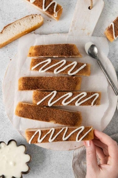 Gluten-free cinnamon breadsticks on a platter, with a hand picking up a breadstick