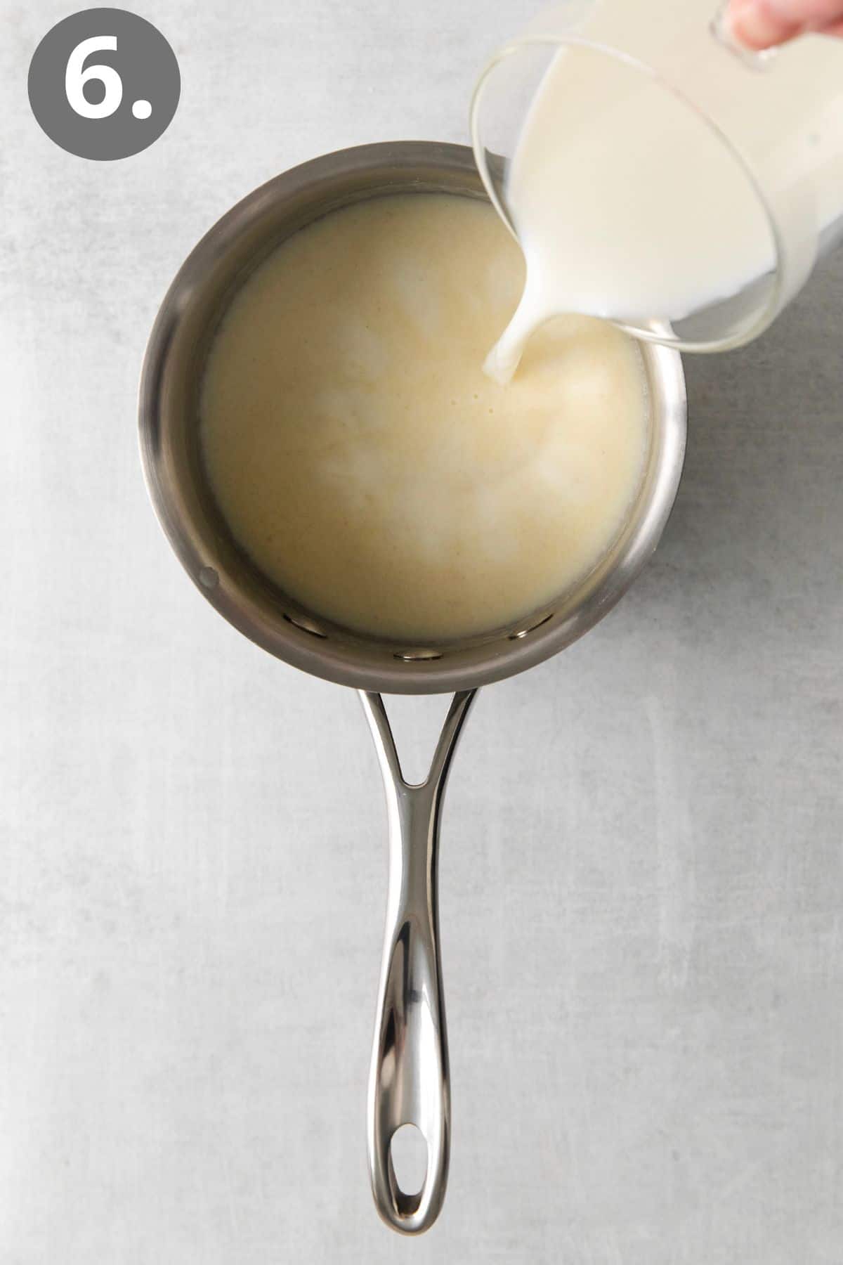 Milk being poured into a saucepan with melted butter and gluten-free flour