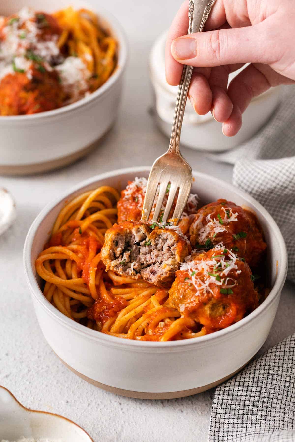 A hand using a fork to pick up a meatball and spaghetti