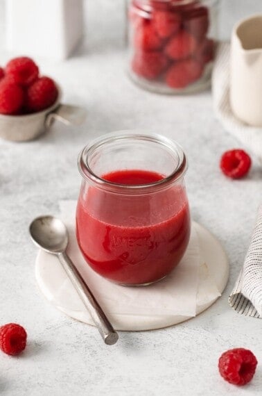 A glass jar filled with raspberry coulis, with a serving spoon next to it