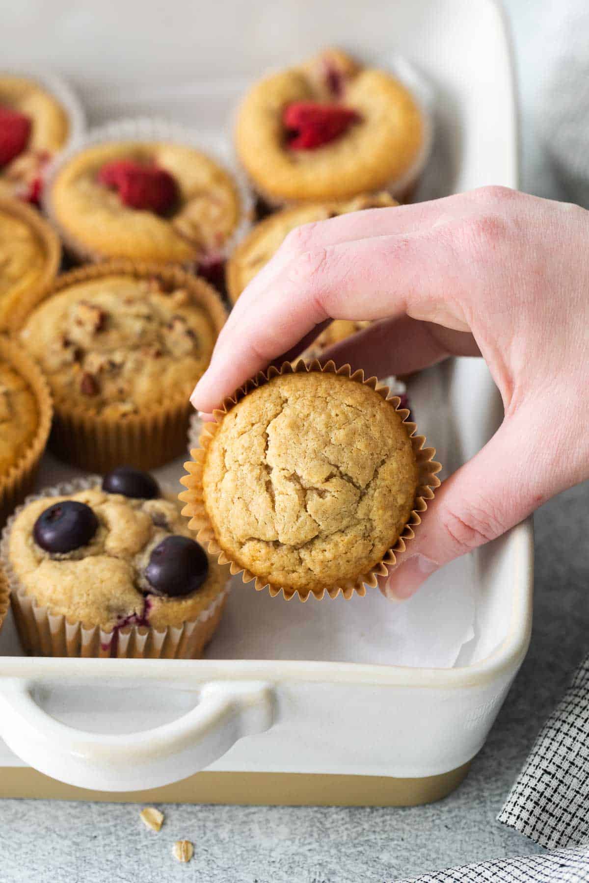 A hand reaching for a oat flour muffin in a baking dish