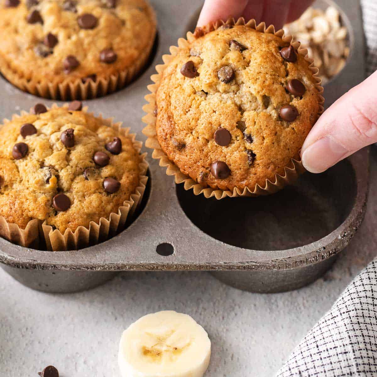 Oat flour banana muffins in a muffin tin, and a hand taking one out