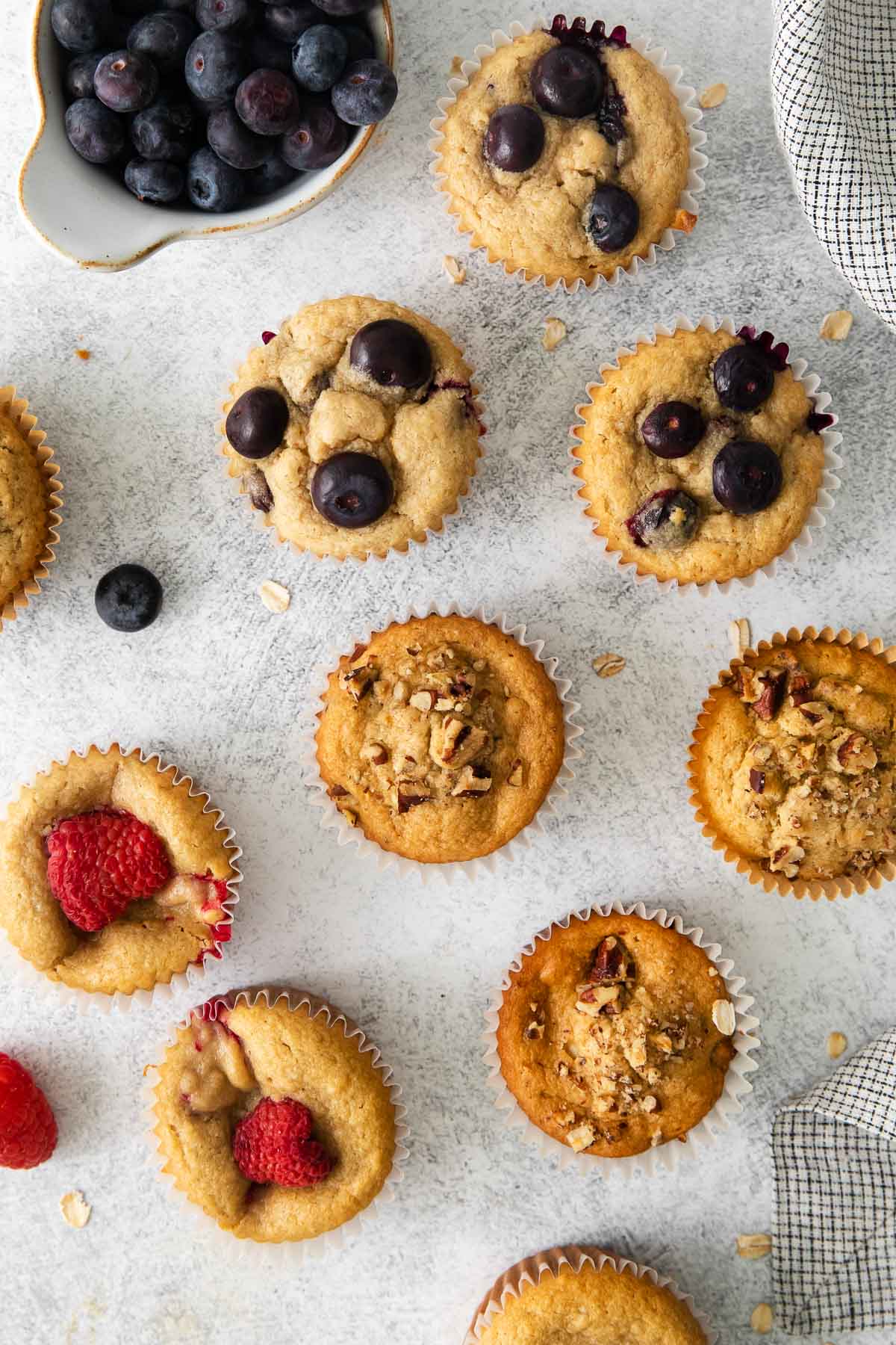 Oat flour muffins spread on a counter top with fruit around them