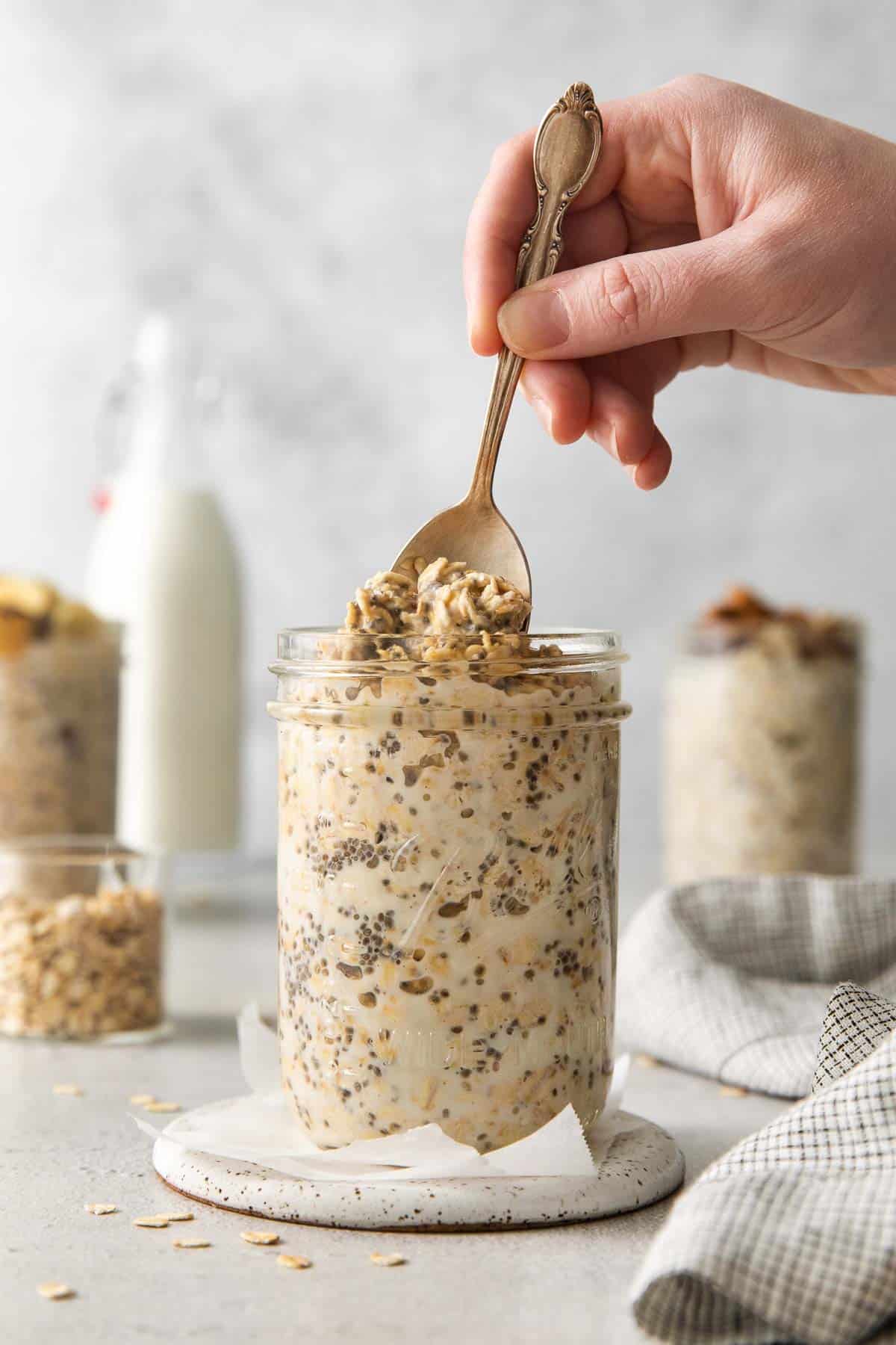 A side view of gluten-free overnight oats in a mason jar, with a hand sticking a spoon in the top