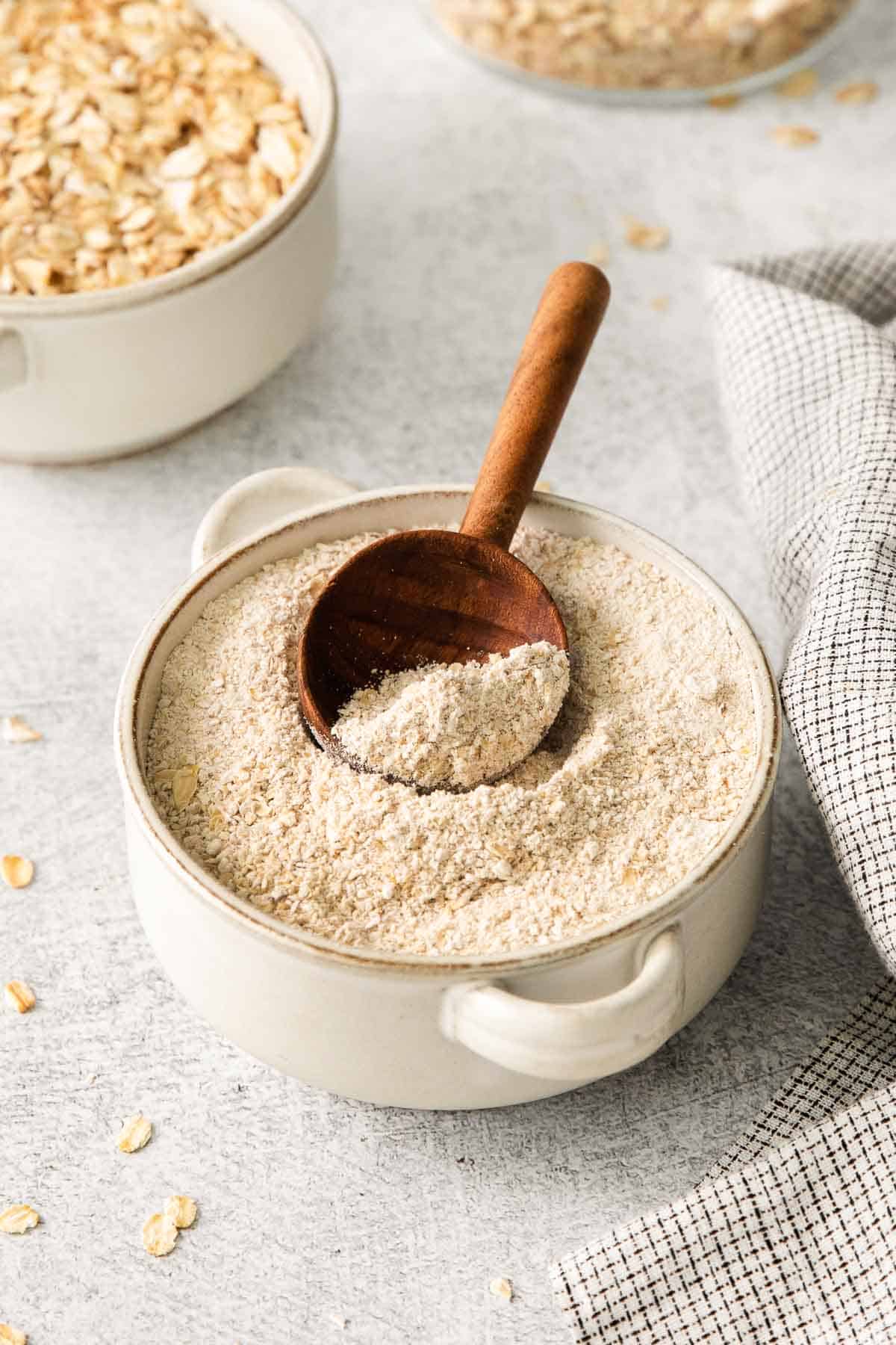 Gluten-free oat flour in a bowl with a wooden spoon in it