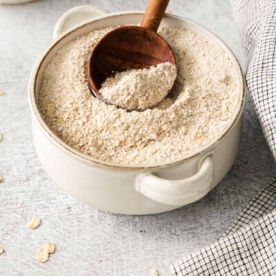 Gluten-free oat flour in a bowl with a wooden spoon in it