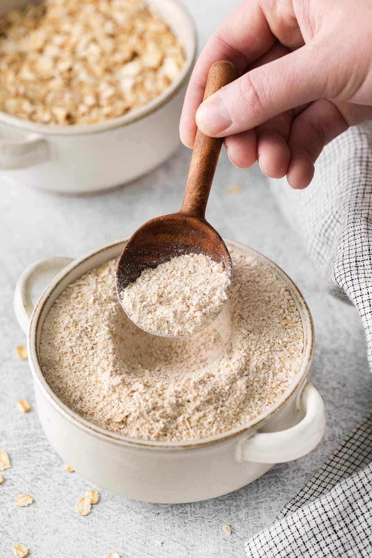 A hand holding a spoon and scooping up gluten-free oat flour from a bowl