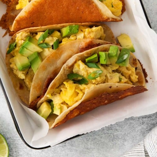 a close up view of breakfast tacos in a baking dish with parchment paper