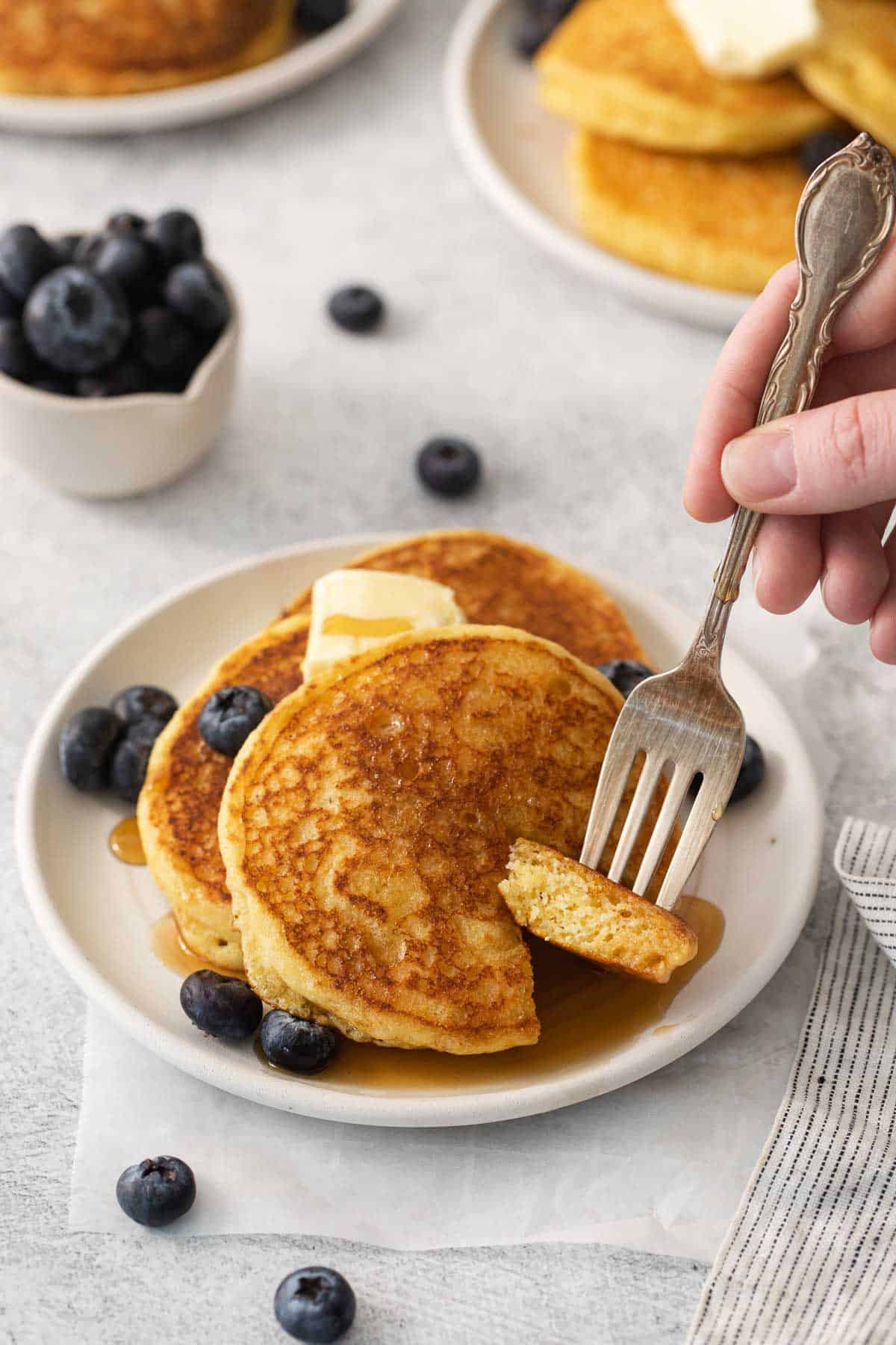 Cornmeal pancakes on a plate with a fork taking a bite out of it