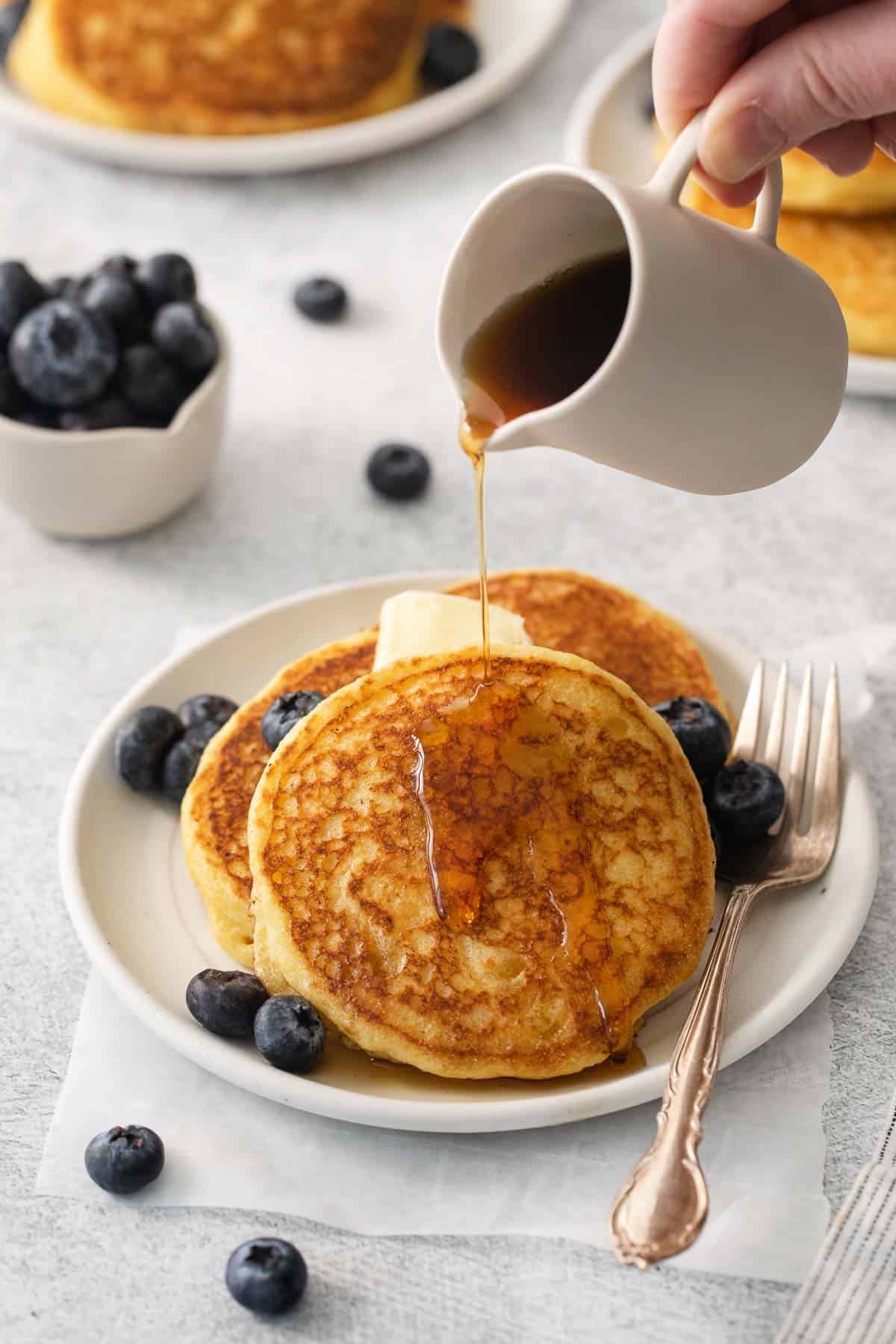 Cornmeal pancakes on a plate and a hand pouring syrup over the top