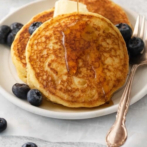 Cornmeal pancakes on a plate with blueberries and a pat of butter on top