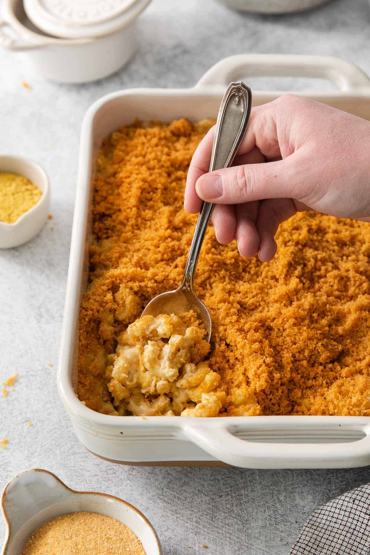 A hand scooping mac and cheese out of a baking dish