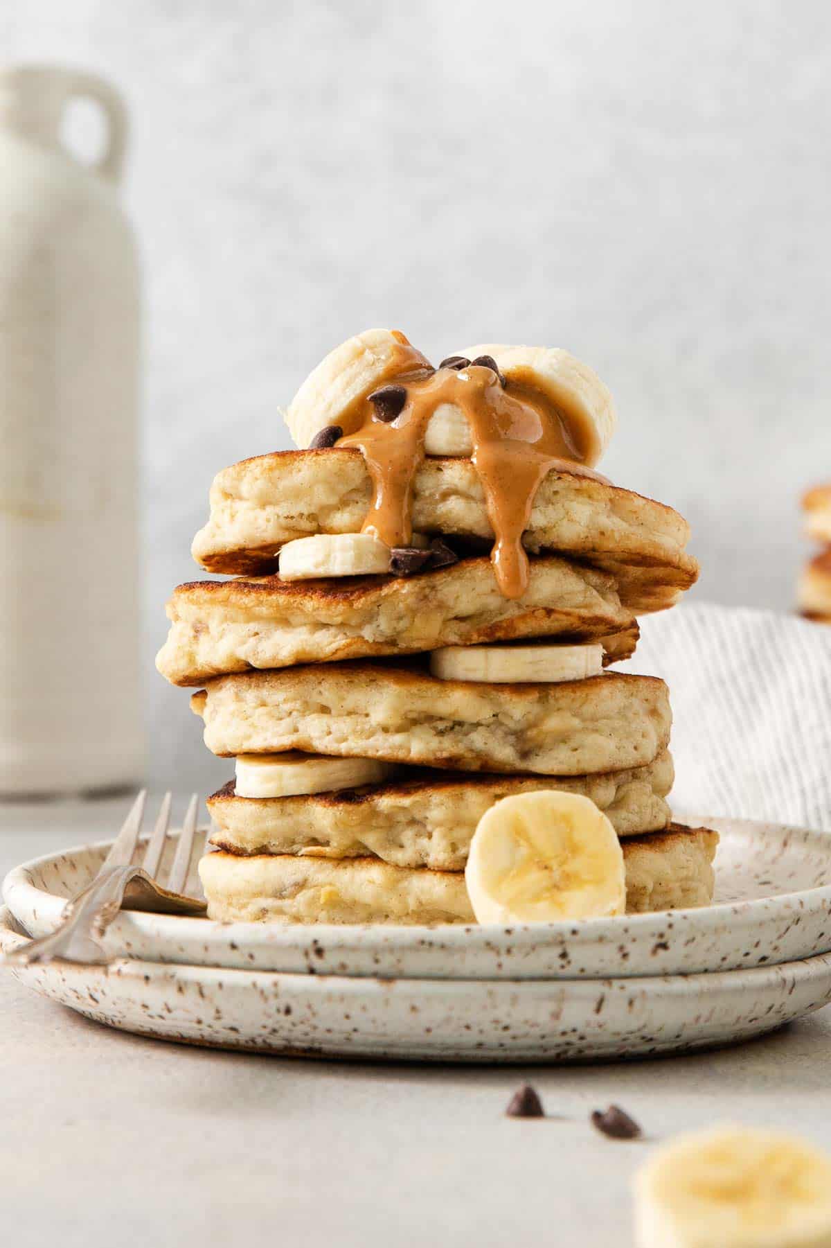 Gluten-free banana pancakes stacked on a plate with a drizzle of peanut butter and banana slices on top