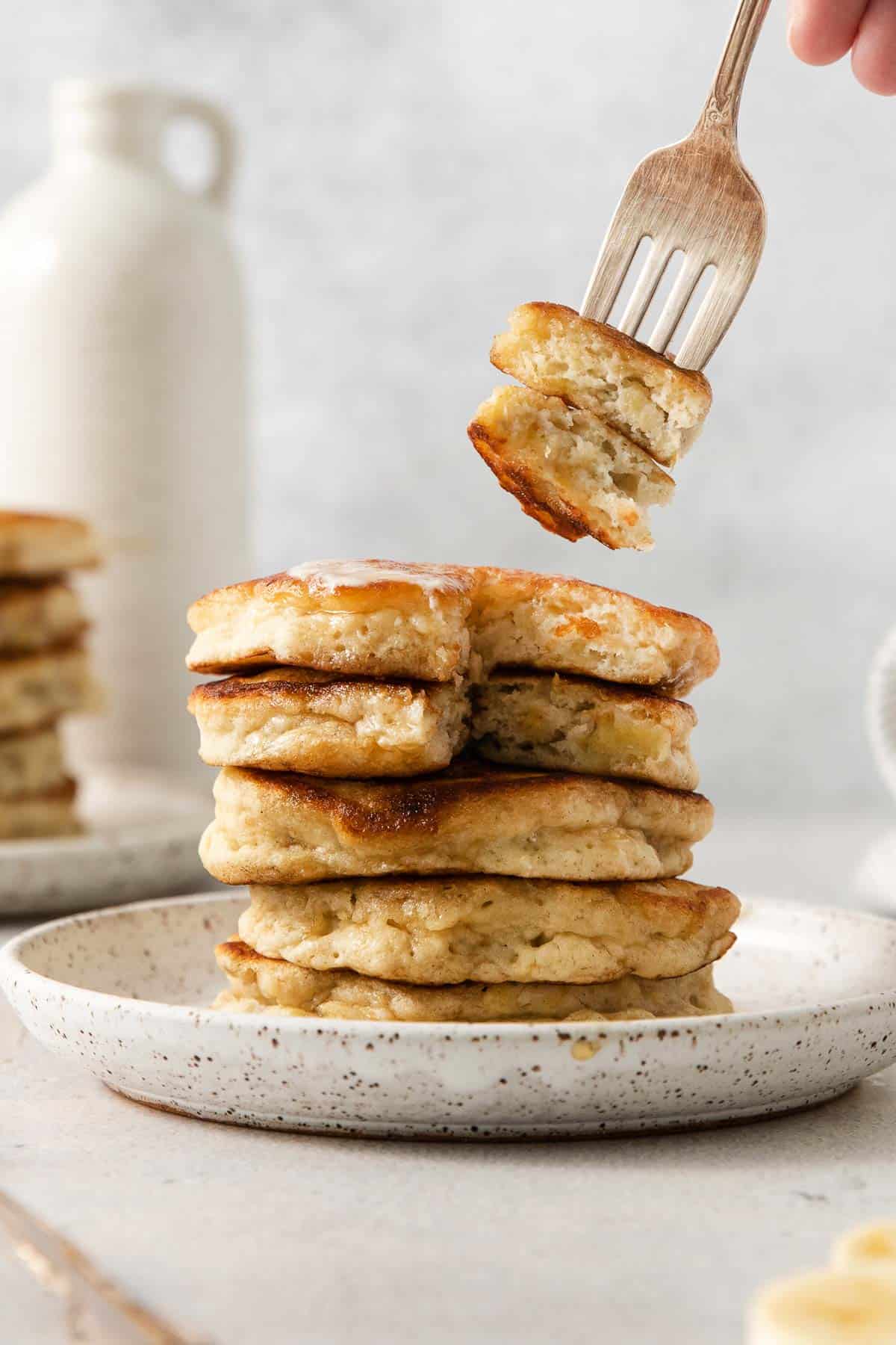 Gluten-free banana pancakes stacked on a plate with a fork taking a bite out of them