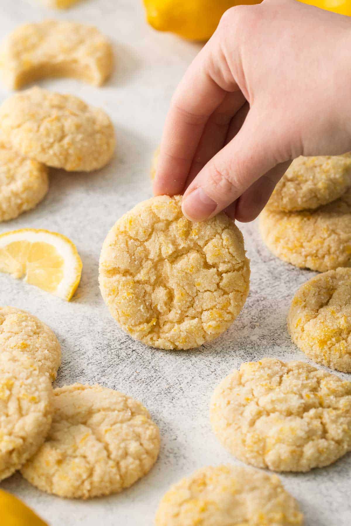 Lemon cookies on parchment paper with a wedge of lemon and a hand picking up a cookie
