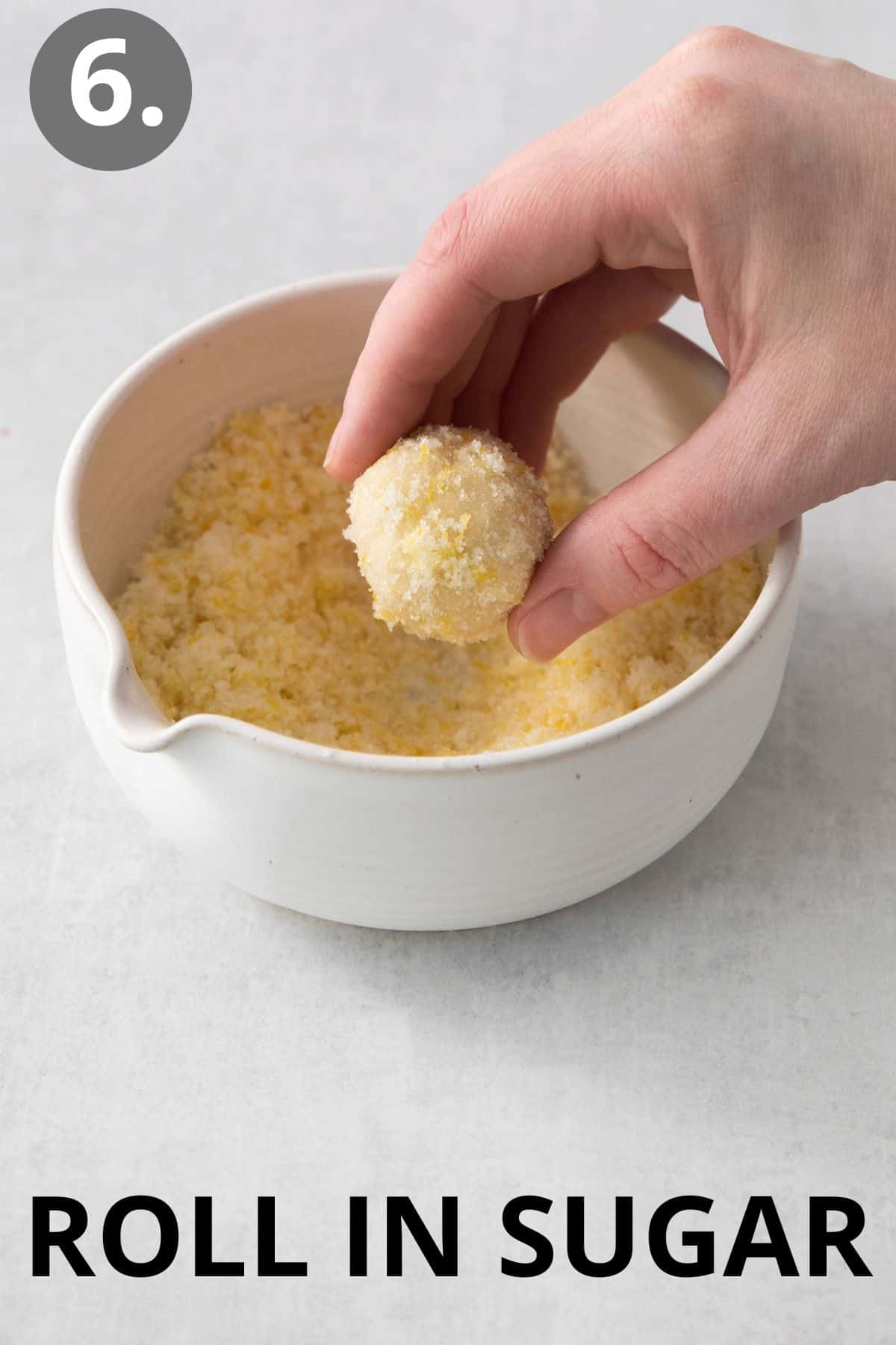 Lemon cookie dough ball rolled being rolled in a bowl of sugar